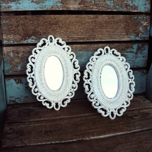 May include: Two white oval mirrors with ornate frames, set against a rustic wooden background with blue paint.