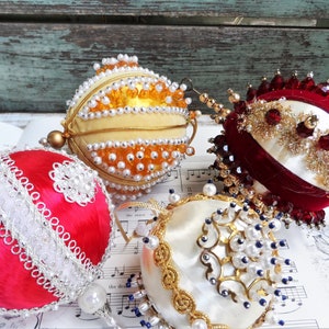 May include: Four vintage Christmas ornaments with a white background. The ornaments are covered in beads and sequins. One ornament is red, one is white, and two are yellow.