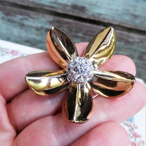 May include: A gold-tone flower brooch with a clear rhinestone center. The flower has five petals and is a classic design.