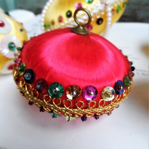May include: A bright pink satin Christmas ornament with a gold trim and colorful sequins. The ornament has a loop at the top for hanging.