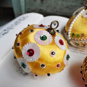 May include: A gold Christmas ornament covered in white and iridescent sequins with red, green, and silver accents.