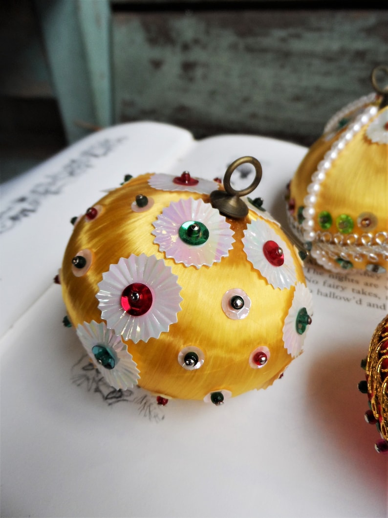 May include: A gold Christmas ornament covered in white and iridescent sequins with red, green, and silver accents.