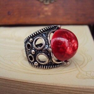 May include: A silver ring with a red, marbled stone set in a decorative, circular design.