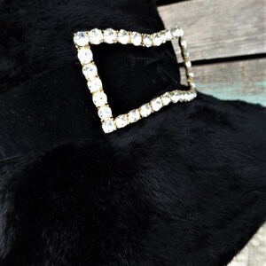 May include: A black fur hat with a large, rectangular rhinestone buckle.