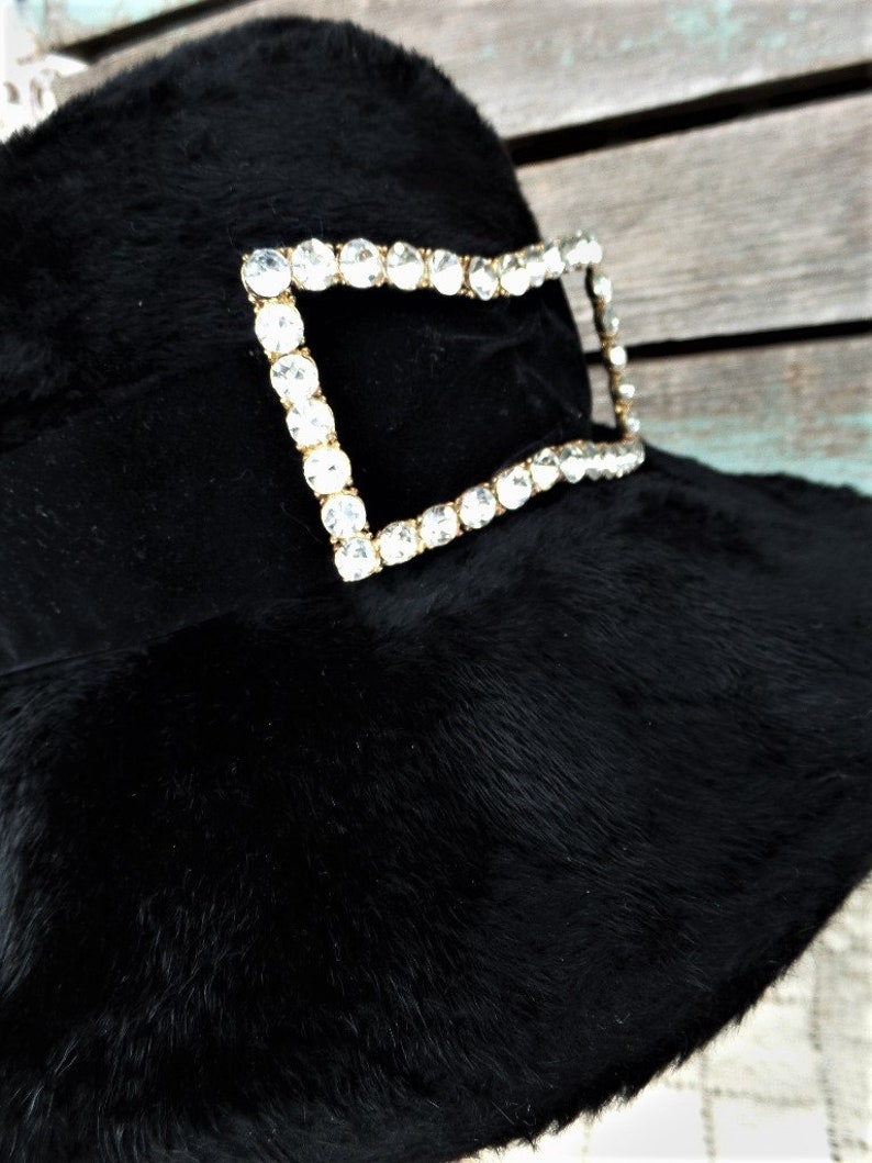 May include: A black fur hat with a large, rectangular rhinestone buckle.