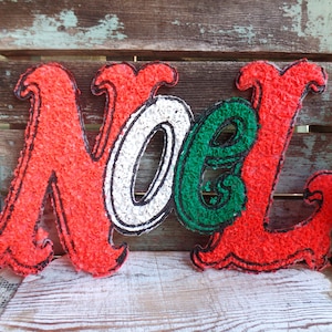 May include: Red, white, and green Christmas decoration with the word "NOEL" in a festive font.