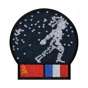 May include: A blue and white embroidered patch depicting a snow globe with a figure inside. The snow globe is topped with a red and white flag with a hammer and sickle symbol and a blue, white, and red flag.