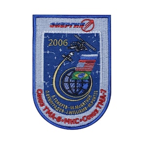 May include: A blue and white embroidered patch with the text "Soyuz TMA-8 - MKC - Soyuz TMA-7" and "2006" in the centre. The patch also features a globe with the flags of Russia, Brazil, and the United States.