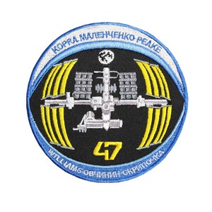 Puede incluir: Parche bordado que representa una estación espacial con paneles solares amarillos y el número 47. El parche tiene un borde azul con texto en idioma extranjero.