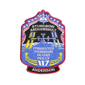 Puede incluir: Un parche bordado azul y blanco con un borde rojo. El parche presenta una lanzadera espacial, la Estación Espacial Internacional y los nombres de los astronautas: Sturckow, Archambault, Forrester, Swanson, Olivas, Reilly y Anderson. El número 117 también está en el parche.