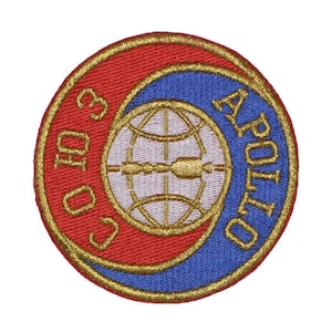 Pu&ograve; includere: Una toppa rotonda ricamata con sfondo rosso e blu. La toppa presenta un globo dorato con una freccia stilizzata e il testo "APOLLO 10" in oro.