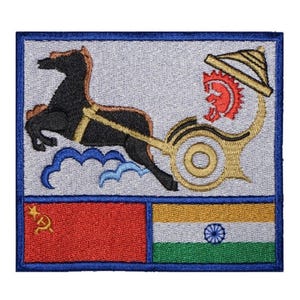 May include: An embroidered patch with a blue border, featuring a white background with a black horse pulling a chariot with a red and gold design. The bottom half of the patch is divided into two sections, one red with a hammer and sickle and the other with the Indian flag.