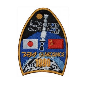 May include: A blue and black embroidered patch featuring a space station, a Japanese flag, a Soviet flag, and the text "フタバ GLAVKOSMOS 1990".