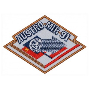 Op de afbeelding: Een witte, ruitvormige patch met een bruine rand. De patch heeft de tekst "AUSTRO-MIR 91" en een illustratie van een blauw-witte vlag met een wereldbol en een pijl die naar rechts wijst.