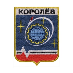 May include: A blue and red embroidered patch with a gold border. The patch features a white stylized rocket, a blue globe with a gear around it, and three white stars. The text "КОРОЛЁВ" is written in black at the top of the patch.