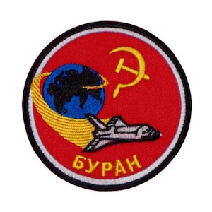 May include: A red, white, and black embroidered patch with a yellow sickle and hammer, a blue globe, a yellow orbit, a white space shuttle, and the text "БУРАН" in white.