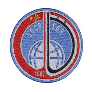 Puede incluir: Un parche redondo bordado con un diseño rojo, blanco y azul. El parche presenta las palabras "CCCP" y "SAR" en letras blancas, junto con un diseño de globo terráqueo y el año "1987".