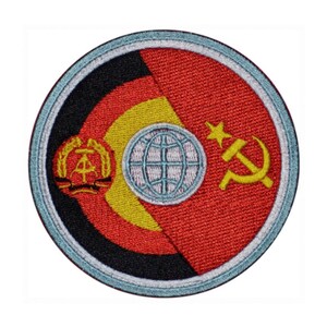 May include: A round embroidered patch with a red, yellow, and black design. The patch features a globe with a hammer and sickle on the right side and a symbol with a wreath on the left side.