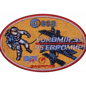 May include: A yellow oval patch featuring a blue and white astronaut in a spacesuit, a space station, and the text "EUROMIR 95 95 ЕВРОМИР" in red and white. The patch also includes the ESA logo and the text "ЭНЕРГИЯ" in Russian.