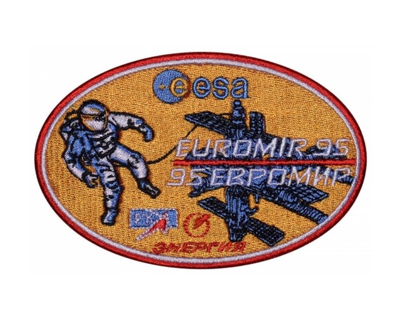 May include: A yellow oval patch featuring a blue and white astronaut in a spacesuit, a space station, and the text "EUROMIR 95 95 ЕВРОМИР" in red and white. The patch also includes the ESA logo and the text "ЭНЕРГИЯ" in Russian.