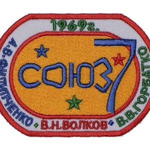 May include: A red, white, and green embroidered patch with the text "СОЮЗ 7" in blue and the text "В.В.ГОРБАТКО - А.С.ОЛЬШЕНКО - В.Н.ВОЛКОВ" in green. The patch also includes the text "1969.2." in green.