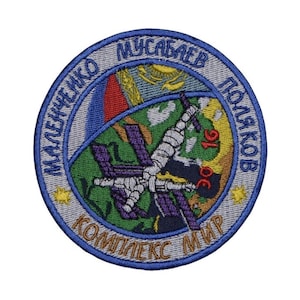 Könnte beinhalten: Ein blauer und grauer gestickter Aufnäher mit dem Text "МАЛЕЧЕНКО МУСАБАЕВ ПОЛЯКОВ КОМПЛЕКС МИР" und einer Darstellung einer Raumstation, die die Erde umkreist.