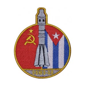 May include: A round embroidered patch featuring a red and white Cuban flag on the right and a red Soviet flag with a hammer and sickle on the left. A silver rocket ship is in the centre of the patch. The text "СОЮЗ-38" is at the bottom of the patch.