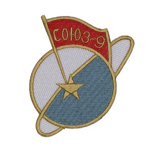 May include: Embroidered patch featuring a design with a red flag, a gold star, and a blue and white circular shape. The flag has the text "СОЮЗ-9" in gold. The patch has a gold border.