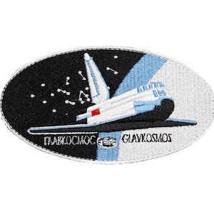 May include: An oval patch with a space shuttle design. The patch features the Cyrillic text "ГЛАВКОСМОС" and the English text "GLAVKOSMOS". The design includes a black background with stars, light blue and white sections, and a white shuttle.