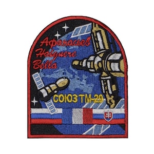 Op de afbeelding: Een blauwe en zwarte geborduurde patch met een spaceshuttle en de tekst "Soyuz TM-29" en "Афанасьев  Haigisere Bella".