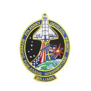 Op de afbeelding: Een blauwe en gele geborduurde patch met een spaceshuttle die de ruimte in schiet. De patch heeft de namen "Curbeam, Polansky, Fuglesang, Williams, Higginsbotham, Oefelein, Patrick" rond de rand.