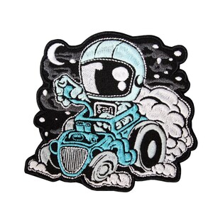 Puede incluir: Un parche bordado con un astronauta de dibujos animados conduciendo un hot rod azul con humo blanco saliendo del escape. El astronauta lleva un casco blanco y una máscara facial negra. El fondo es negro con estrellas blancas.