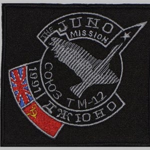 May include: Black embroidered patch with white text and a spacecraft design. The patch includes the text "THE JUNO MISSION", "СОЮЗ TM-12 ДЮНО", and a flag design with the year "1991".
