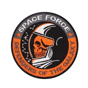 May include: Orange and black embroidered patch featuring a skull wearing a helmet and the text "Space Force Defenders of the Galaxy".