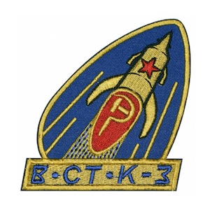 Puede incluir: Un parche bordado azul y dorado con un cohete y una estrella roja. El texto "B-CT-K-3" está debajo del cohete.
