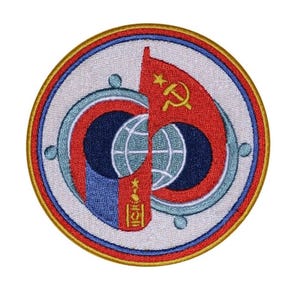 May include: A circular embroidered patch with a red, white and blue design. The centre features a stylised globe with a red star and a hammer and sickle. The outer ring is blue with a white border and a gold border.