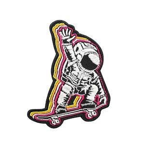 May include: An embroidered patch of an astronaut riding a skateboard. The astronaut is wearing a white spacesuit with a black helmet. The skateboard is outlined in yellow, orange, and pink.