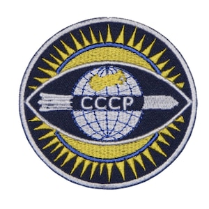 May include: A blue and yellow embroidered patch featuring a globe, a missile, and the text "CCCP" in the centre. The globe is surrounded by a ring of yellow sun rays.