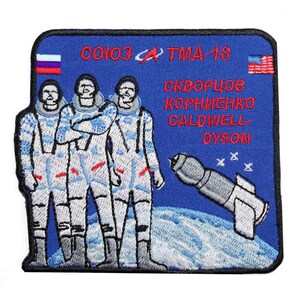 Puede incluir: Un parche bordado azul con el texto "CO103 TMA-18" y los nombres "SKVORTSOV KORNIENKO CALDWELL DYSON". El parche presenta tres astronautas con trajes espaciales, una nave espacial y las banderas de Rusia y los Estados Unidos.
