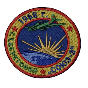 May include: A yellow and red embroidered patch with a green and red aeroplane flying over a blue and white globe with a yellow sun rising above it. The text "1968 г. Г.Т. БЕРЕГОВОЙ  СОЮЗ-3" is around the globe.