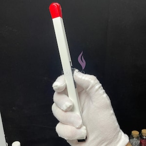 May include: A white and red electric lighter held in a gloved hand. The lighter has a rectangular shape with a red top and a white body. The lighter is designed to resemble a large match.