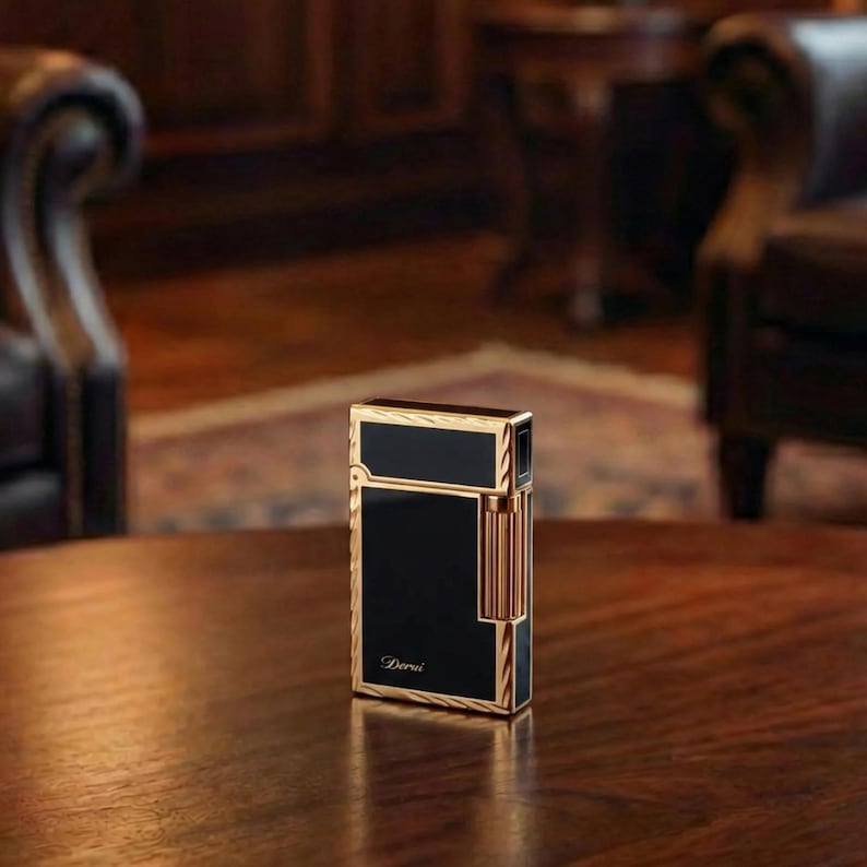 May include: A black and gold lighter with the word "Derui" printed on the front. The lighter has a rectangular shape with gold trim and accents. The lighter is on a wooden table.