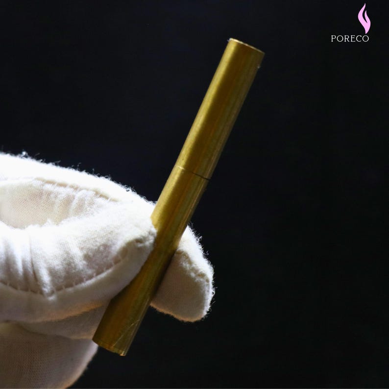 K&ouml;nnte beinhalten: Ein goldfarbenes, zylindrisches Metallobjekt, m&ouml;glicherweise ein Stift oder Werkzeug, wird in einer wei&szlig; behandschuhten Hand vor dunklem Hintergrund gehalten. Das Objekt hat ein segmentiertes Design und eine gl&auml;nzende Oberfl&auml;che. Das Logo "PORECO" ist sichtbar.