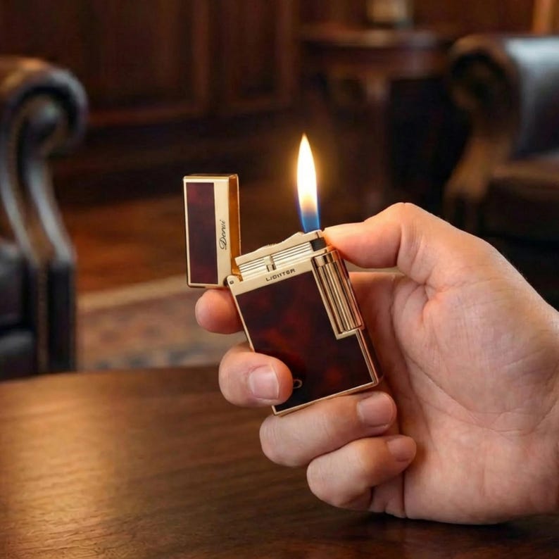 May include: A gold and brown lighter with a flame. The lighter has a rectangular shape with a hinged lid. The body of the lighter has a brown, tortoiseshell-like pattern. The lighter is held in a hand.
