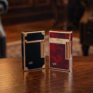May include: Two luxury lighters, one black and one red, with gold-coloured accents. The black lighter has a gold-coloured 'D' logo. The red lighter has the text "Derui Lighter" in gold. Both lighters are on a wooden surface.