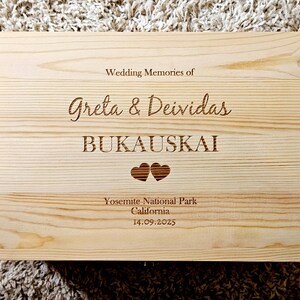 Puede incluir: Una caja de madera clara con texto grabado. El texto dice "Wedding Memories of Greta & Deividas Bukauskai" con dos símbolos de corazón y "Yosemite National Park California 14.09.2025". La caja tiene una veta de madera natural.