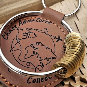 May include: A brown leather keychain with a silver ring. The keychain features the words "Chase Adventures" and "Collect" with a world map and airplane graphic. A stack of gold-coloured metal rings is attached.