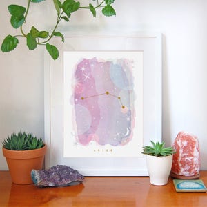 May include: A framed watercolor print of the Aries constellation with gold stars and a pink and purple background. The text "ARIES" is printed below the constellation.