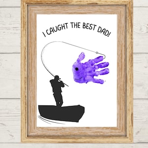 Könnte beinhalten: Gerahmter Kunstdruck mit einem hellen Holzmaserungsrahmen. Der Druck zeigt eine Silhouette einer Person, die von einem Boot aus angelt, mit einem lila Handabdruck in Form eines Fisches. Der Text lautet: "Ich habe den besten Papa gefangen!"