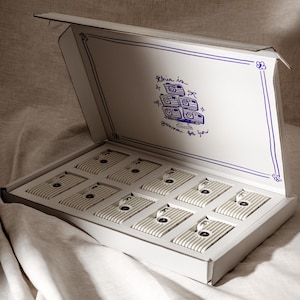 May include: Open white box with a blue line border and a blue illustration of cameras. Inside are eight rectangular, off-white objects with black details. The text "This is gonna be fun" is written in blue.